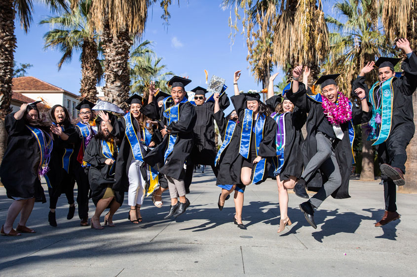 SJSU graduates jumping up in the air.