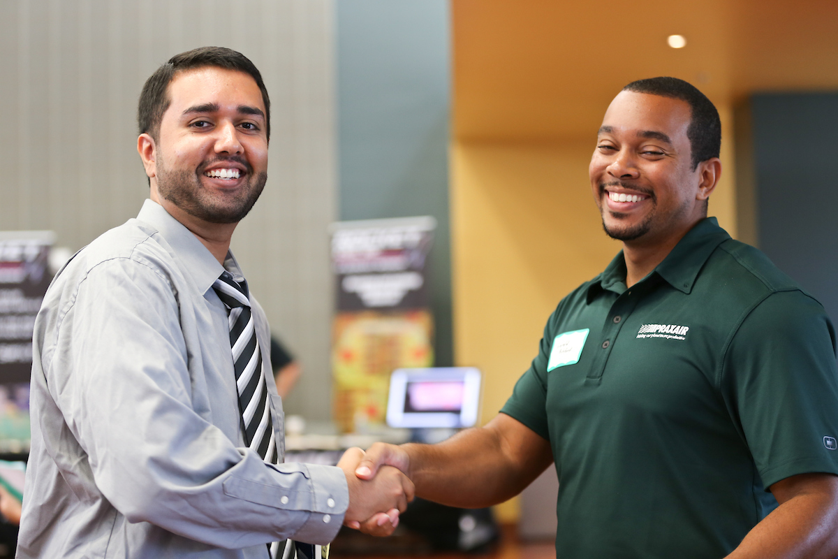 two males shaking hands and looking at the camera and smiling