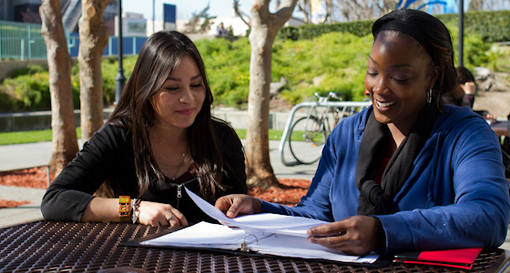 Two people talking outside over a binder of course information.