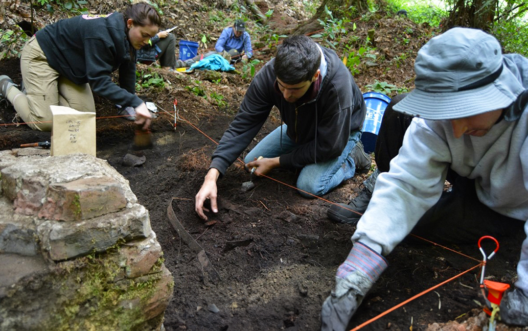 Anthropology students crouch down on the dirt as they dig up a targeted area on the ground.