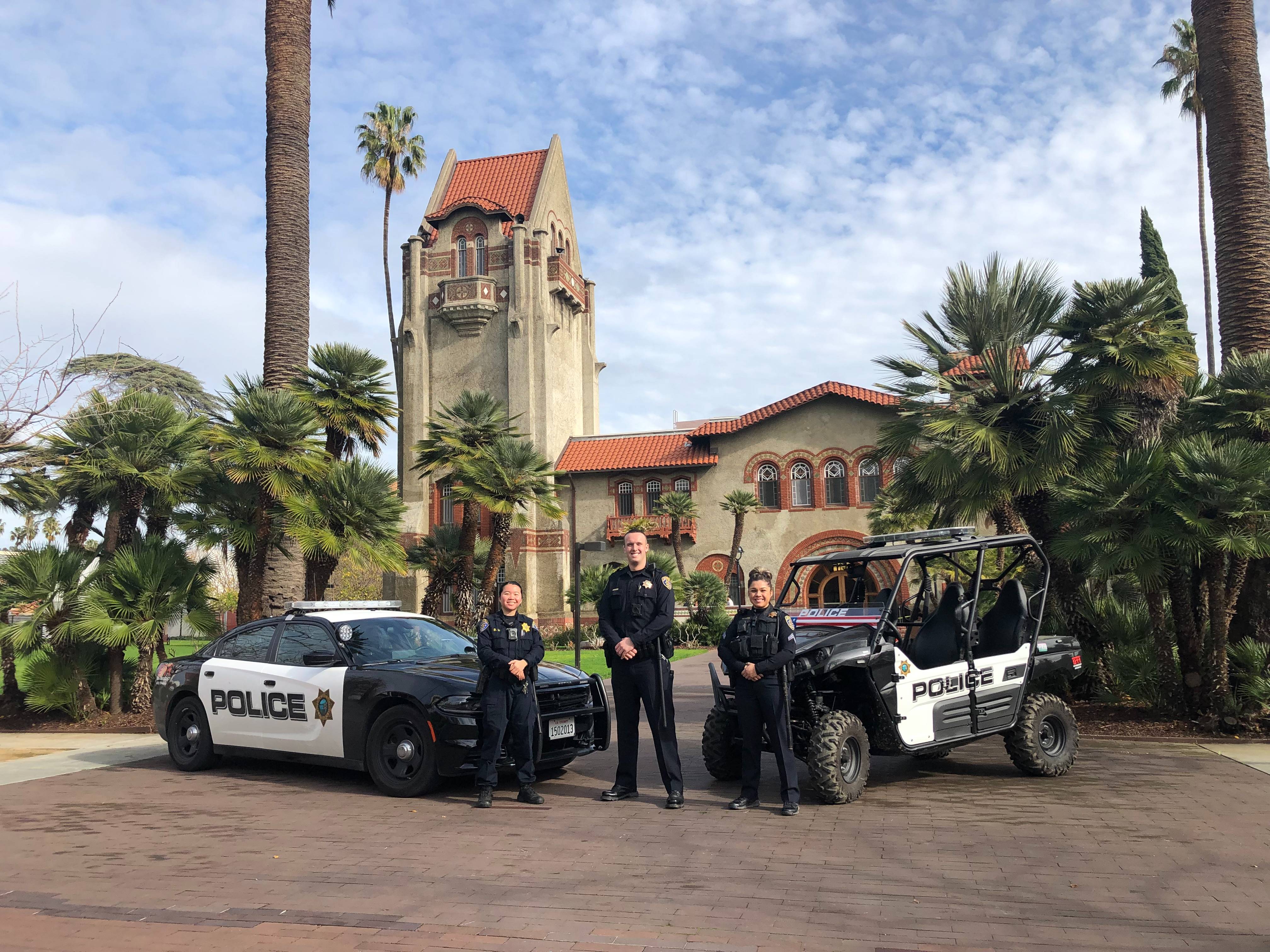 Male university police officer stands by his car smiling