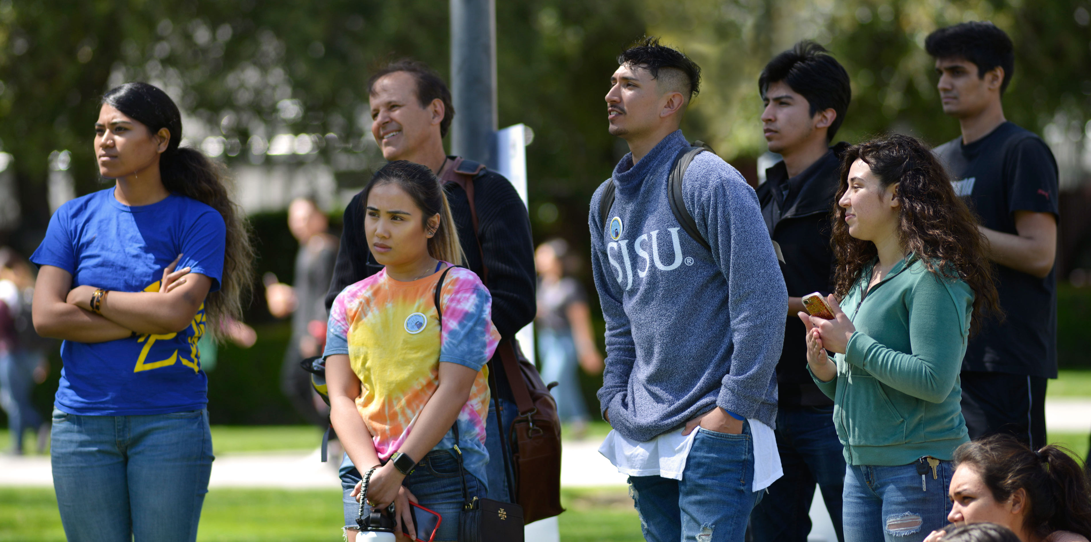 SJSU community members standing and listening to a speech.