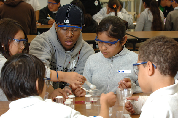 person leads science project with child and other children crowded around