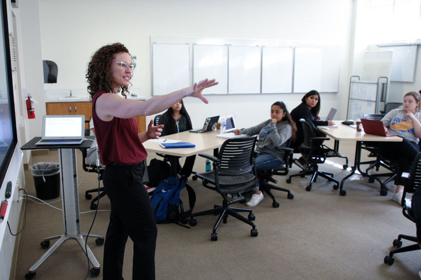 A professor holds out her arm towards the classroom as she speaks.