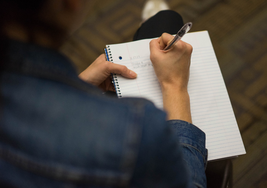 Photo by James Tensuan of a hand holding a pen and writing on a notepad