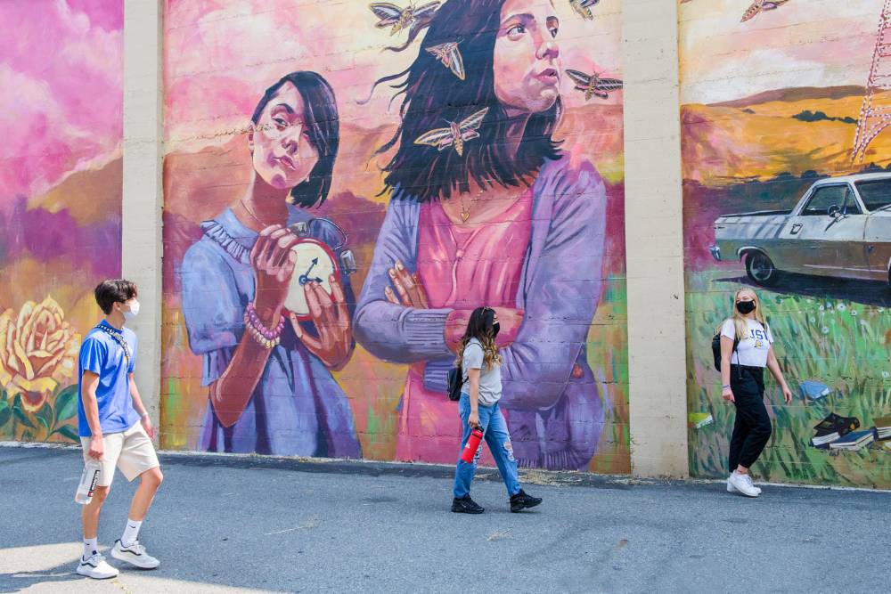 Students in masks walking by a color mural.